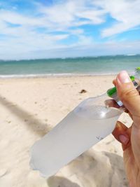 Midsection of person holding bottle on beach against sky