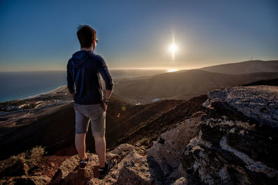 Rear view of man looking at mountains against sky during sunset