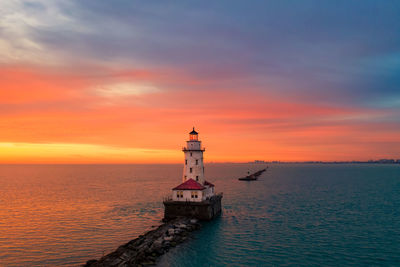 Lighthouse by sea against sky during sunset