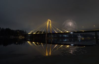 Illuminated bridge over river against sky at night