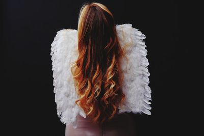 Rear view of woman in costume standing against black background