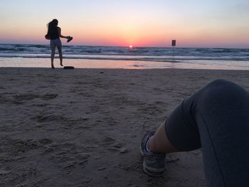 Low section of woman at beach against sky during sunset