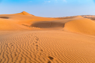 Sand dunes with footprints in them under the blue sky with soft haze on the distant horizon.