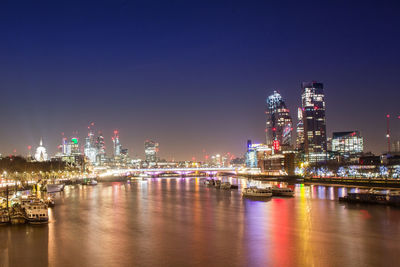 Illuminated buildings by river against sky at night