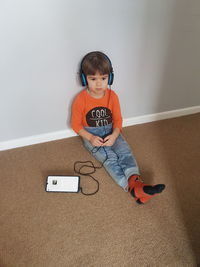 High angle view of boy listening music while sitting on floor against wall