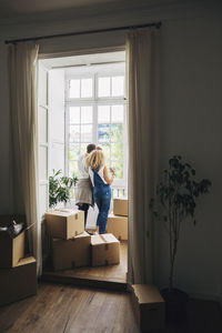 Rear view of couple looking through window while standing in new house seen through doorway