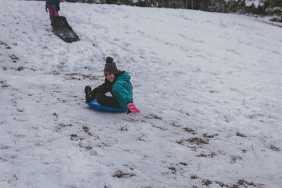 Full length of girls sitting on bobsled in snow