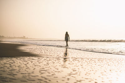 Rear view of man walking on beach against clear sky