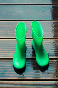 High angle view of green rubber boots on wet floorboard