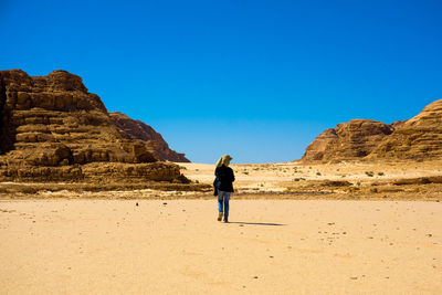 Rear view of person walking at desert against blue sky