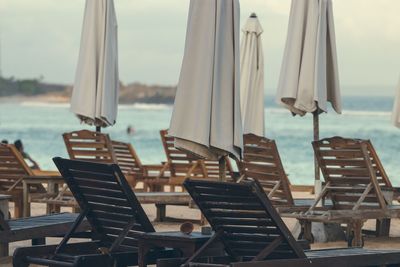 Empty chairs and tables at beach against sky