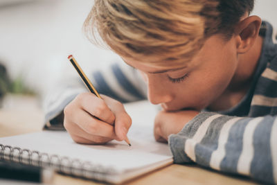 Close-up of boy making sketch on note pad at table