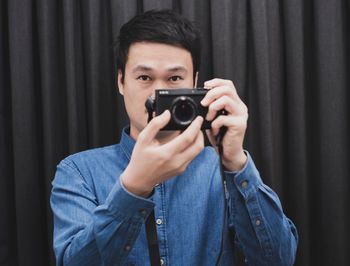 Portrait of man photographing against black curtain