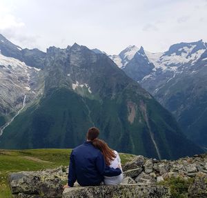 Rear view of couple sitting on rock against mountains