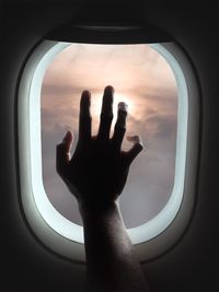 Low angle view of hand touching window against sky