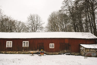 Lesbian mothers with daughter against cottage during winter