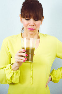 Woman having drink while standing against wall