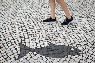 Low section of woman walking on cobblestone street