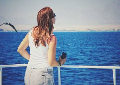 Woman using mobile phone by sea against sky