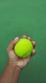 Cropped image of person holding tennis ball against green tennis court