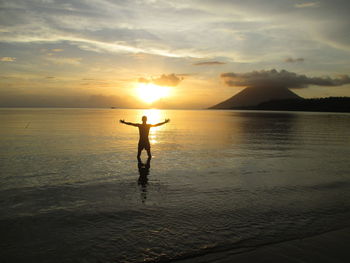 Silhouette man standing on beach against sky during sunset