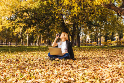 Woman using laptop while sitting on leaves in park