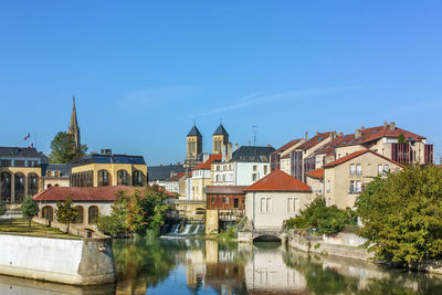 River by buildings in city against blue sky