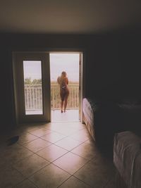 Rear view of woman standing by window at home