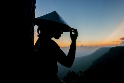 Silhouette woman wearing asian style conical hat against sky during sunset