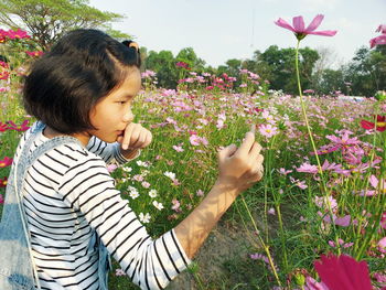 Side view of girl photographing flowers with mobile phone growing in park