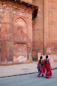 Full length rear view of women walking on street against red fort