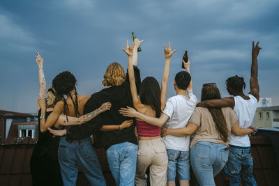 Rear view of multiracial young men and women gesturing with arms raised on rooftop at dusk