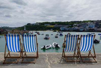 Deck chairs at lakeshore against sky