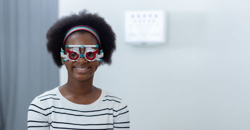 Portrait of young woman wearing sunglasses against wall