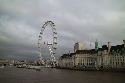 Ferris wheel in city against cloudy sky