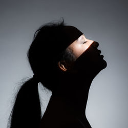 Side view of young woman with eyes closed against gray background