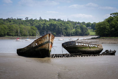 Abandoned boat moored on shore against sky