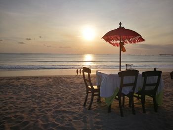 Chairs on beach against sky during sunset