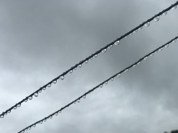 Low angle view of wet wires against sky during rainy season