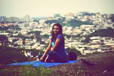 Woman sitting on balcony at city during sunset