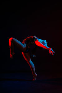 Full length of woman exercising against black background