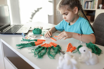 Girl making decoration while by laptop on table at home