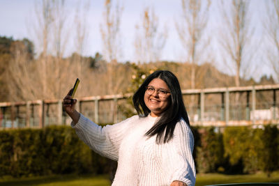 Portrait of smiling young woman standing against trees