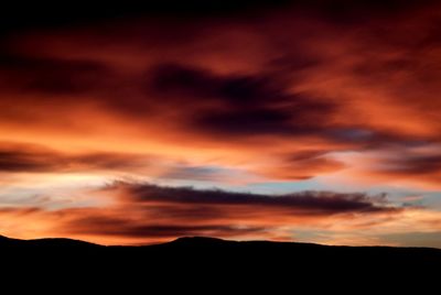 Silhouette landscape against dramatic sky during sunset