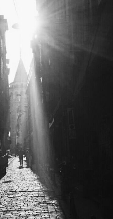 architecture, building exterior, built structure, walking, street, sunlight, the way forward, city, lifestyles, sunbeam, men, cobblestone, sidewalk, lens flare, city life, sun, full length, person