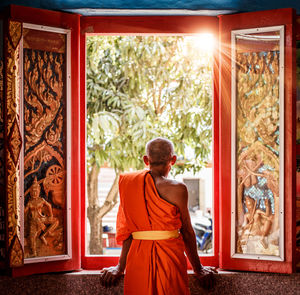 Rear view of monk looking through window at temple