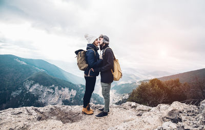 Full length of couple kissing while standing on cliff