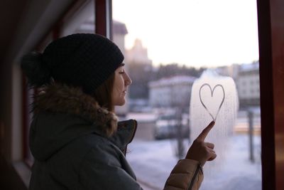 Side view of woman making heart shape on window
