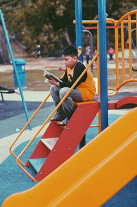 Full length of boy sitting on slide at playground