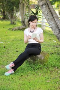 Young woman using phone while sitting on field